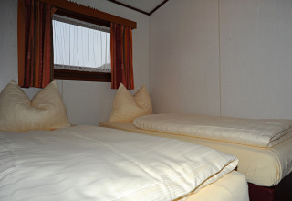 Slaapkamer met twee eenpersoonsbedden, zachte kussens en raam in chalet Waldferienpark Gerolstein 2, Duitsland.