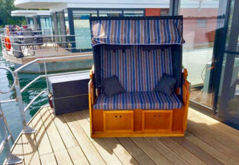 Buitendek van een woonboot met gestreepte zitbank en glazen wand bij Floating 44 in Duitsland.