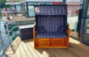 Pont extérieur d'une péniche avec un banc rayé et mur en verre au Floating 44, en Allemagne.