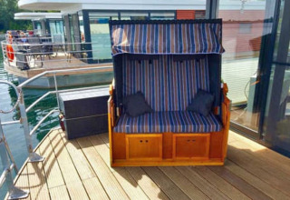 Außendeck eines Hausboots mit gestreifter Sitzbank und Glaswand bei Floating 44, Deutschland.