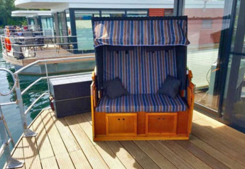 Pont extérieur d'une péniche avec un banc rayé et mur en verre au Floating 44, en Allemagne.