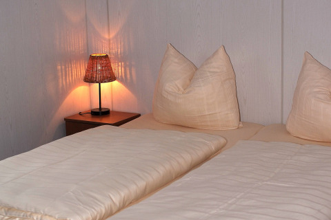 Slaapkamer met twee bedden, zachte kussens, lichte dekens en een brandende lamp in chalet Waldferienpark.