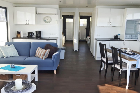 Modernes Wohnzimmer auf Hausboot Floating 44 mit Küche, Esstisch und blauer Couch in Deutschland.