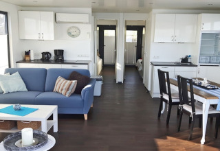 Modernes Wohnzimmer auf Hausboot Floating 44 mit Küche, Esstisch und blauer Couch in Deutschland.