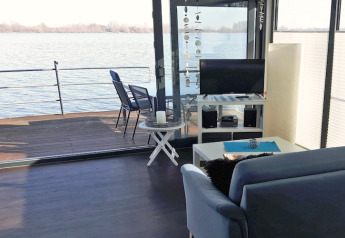 Woonkamer op een woonboot met bank, tv en terras aan het water, gezien op Floating 44 in Duitsland.