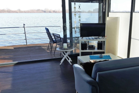 Wohnbereich eines Hausbootes mit Sofa, Fernseher und Terrasse am Wasser, Floating 44 in Deutschland.