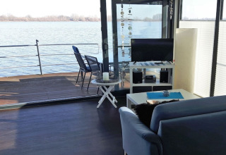 Wohnbereich eines Hausbootes mit Sofa, Fernseher und Terrasse am Wasser, Floating 44 in Deutschland.