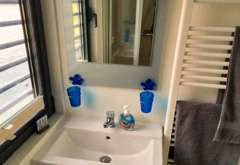 Badkamer op een woonboot met wastafel, spiegel, blauwe bekers en zeeppomp bij Floating 44 in Duitsland.