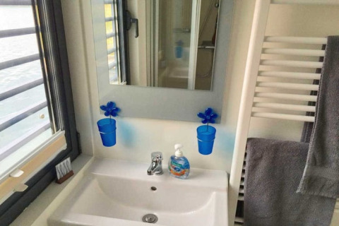 Badezimmer auf einem Hausboot mit Waschbecken, Spiegel, blauen Bechern und Seifenspender in Deutschland.