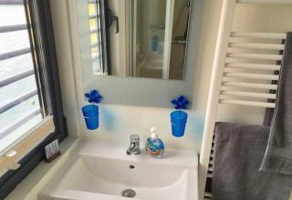 Badezimmer auf einem Hausboot mit Waschbecken, Spiegel, blauen Bechern und Seifenspender in Deutschland.