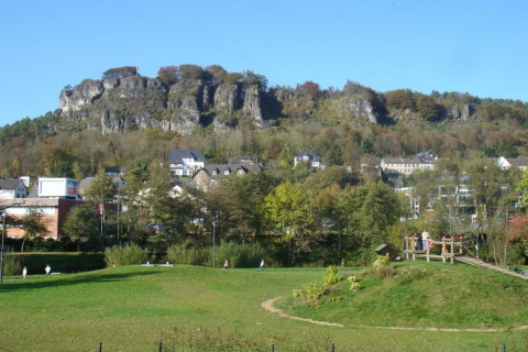 Zicht op groene weides en een dorp onder een rotsheuvel, genomen vanuit Waldferienpark Gerolstein 2, Duitsland.