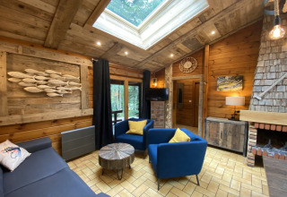 Houten chalet met dakraam, open haard, blauwe zetels en uitzicht op het bos in Frankrijk.