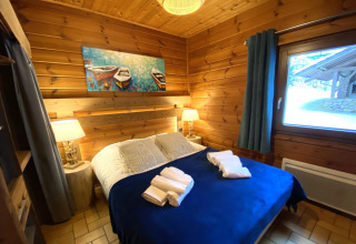 Camera da letto nello chalet di legno LE FISHING LODGE in Francia, con pareti di legno e coperta blu.