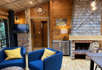 Woonkamer in het LE FISHING LODGE houten chalet in Frankrijk met open haard, blauwe stoelen en gele kussens.
