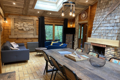 Interieur van houten chalet 'LE FISHING LODGE' in Frankrijk met gezellige zithoek, eetruimte en haard.