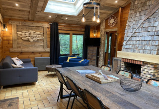 Interior of 'LE FISHING LODGE' wooden chalet in France showing cozy living area, dining table, and fireplace.