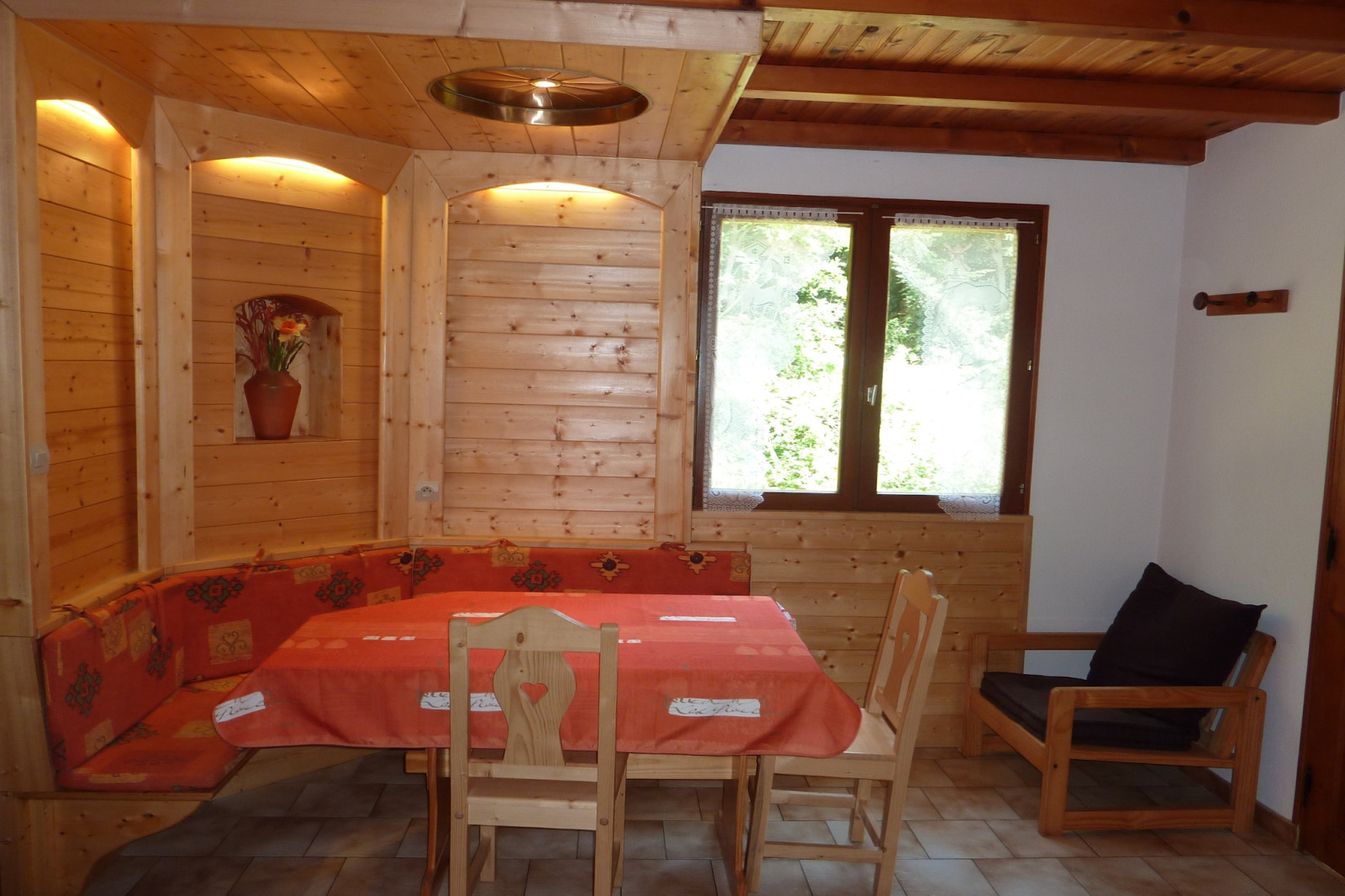 Knusse houten eethoek in chalet 'Ronds Chetys' in Frankrijk met rode tafelkleed en bankzitplaatsen.