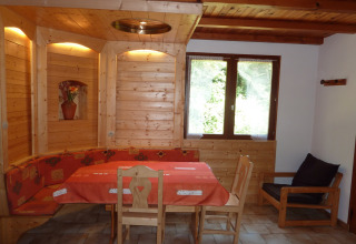 Area pranzo in legno nel chalet «Ronds Chetys» in Francia, con panche e tovaglia rossa decorativa.