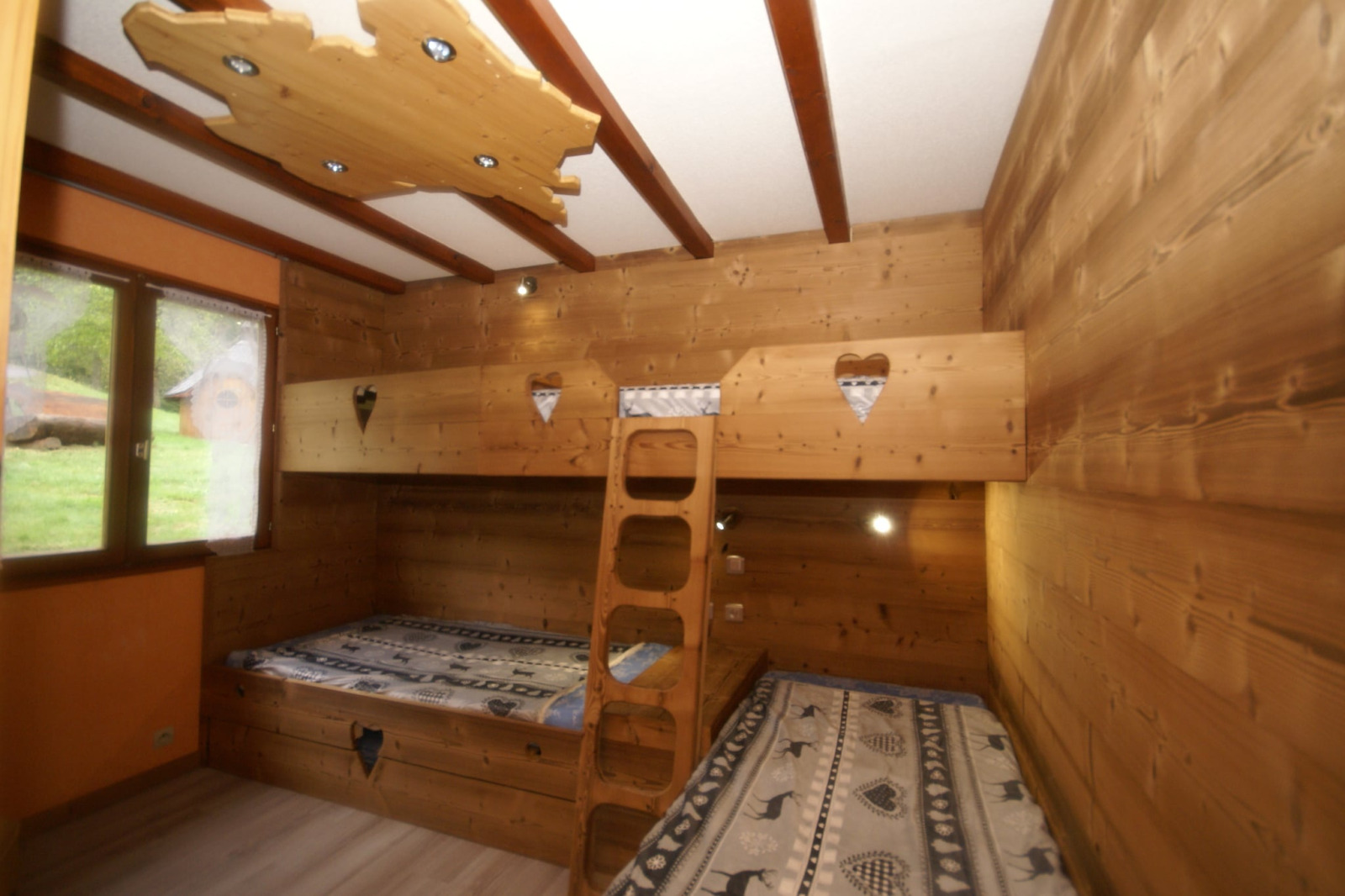 Knusse houten kamer met stapelbedden en hartvormige uitsparingen in chalet Ronds Chetys, Frankrijk.