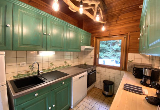 Cozy kitchen in LE FISHING LODGE wooden chalet in France with green cabinets and forest view window.