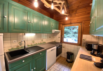 Gezellige keuken in houten chalet LE FISHING LODGE in Frankrijk met groene kastjes en boszicht.