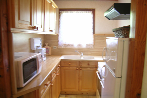 Piccola cucina con mobili in legno, forno a microonde e finestra nello chalet Ronds Chetys, Francia.