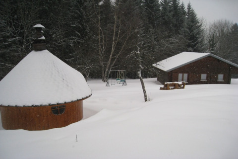 Chalet e casetta barbecue innevati a Ronds Chetys, Francia, circondati da boschi e altalena per bambini.