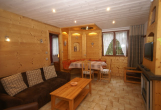 Soggiorno dello chalet 'Ronds Chetys' in Francia con pareti in legno, divano e zona pranzo.