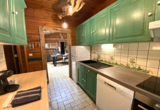 Cucina in legno di LE FISHING LODGE, Francia, con armadi verdi e zona pranzo visibile in fondo.