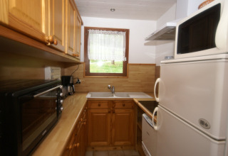 Piccola cucina con mobili in legno, elettrodomestici e finestra nel chalet Ronds Chetys in Francia.