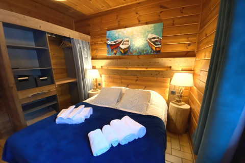 Sfeervolle slaapkamer in houten chalet 'LE FISHING LODGE' in Frankrijk, met tweepersoonsbed en lampen.