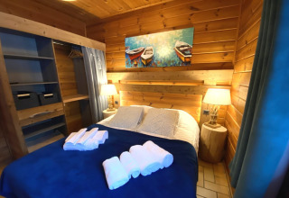 Sfeervolle slaapkamer in houten chalet 'LE FISHING LODGE' in Frankrijk, met tweepersoonsbed en lampen.