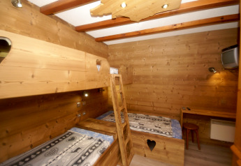 Holzverkleidetes Chaletzimmer in Ronds Chetys, Frankreich, mit Etagenbetten, Schreibtisch und TV.