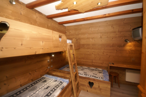 Camera di chalet con pareti in legno a Ronds Chetys, Francia, con letti a castello, scrivania e TV.