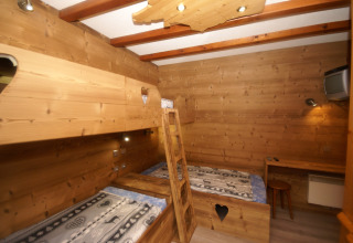 Camera di chalet con pareti in legno a Ronds Chetys, Francia, con letti a castello, scrivania e TV.
