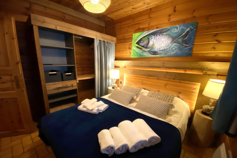 Slaapkamer in LE FISHING LODGE in Frankrijk met houten muren, viskunstwerk en opgemaakt bed.