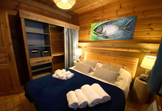 Slaapkamer in LE FISHING LODGE in Frankrijk met houten muren, viskunstwerk en opgemaakt bed.
