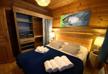 Slaapkamer in LE FISHING LODGE in Frankrijk met houten muren, viskunstwerk en opgemaakt bed.