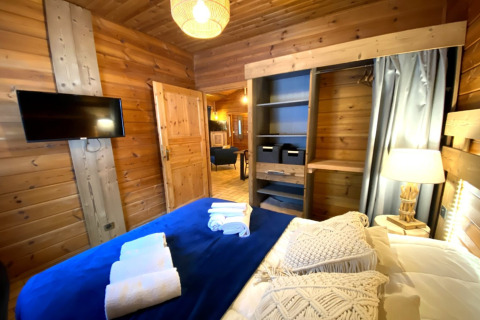 Slaapkamer in het LE FISHING LODGE chalet in Frankrijk, houten muren, TV, open kast en nachtlampje.