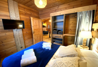 Slaapkamer in het LE FISHING LODGE chalet in Frankrijk, houten muren, TV, open kast en nachtlampje.
