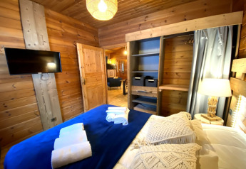 Slaapkamer in het LE FISHING LODGE chalet in Frankrijk met houten interieur, TV, kast en lamp.