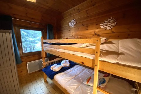 Slaapkamer met stapelbed, houten muren en zicht op een besneeuwd bos in LE FISHING LODGE chalet Frankrijk.