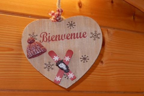 Insegna di legno a forma di cuore con 'Bienvenue', berretto, sci e fiocchi di neve su parete in legno.