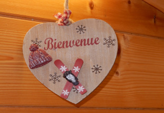 Insegna di legno a forma di cuore con 'Bienvenue', berretto, sci e fiocchi di neve su parete in legno.