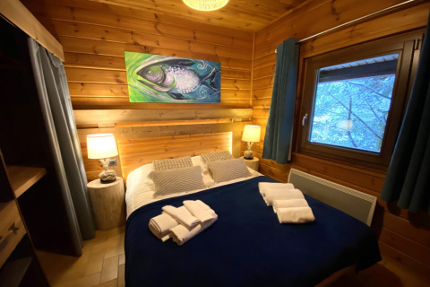 Gezellige slaapkamer in houten chalet met viskunstwerk, tweepersoonsbed en boszicht in Frankrijk.