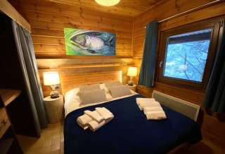Knusse slaapkamer in houten chalet met viskunst, tweepersoonsbed en uitzicht op bos in Frankrijk.