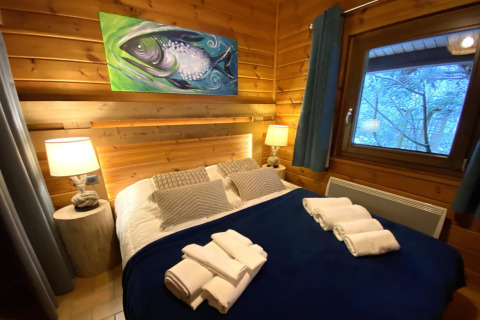 Camera da letto nello chalet LE FISHING LODGE con coperta blu e dipinto di pesce, Francia.