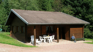 Buitenbeeld van chalet Ronds Chetys met houten gevel, tuinstoelen en bosachtige achtergrond