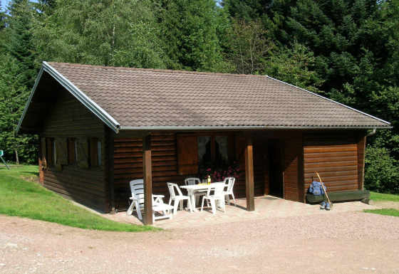 Foto esterna dello chalet Ronds Chetys con struttura in legno, sedie da giardino e foresta sullo sfondo
