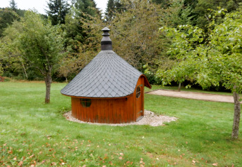 Ein rundes Holzhaus mit dunklem Dach im Grünen bei Chalet 'Ronds Chetys' in Frankreich fotografiert.